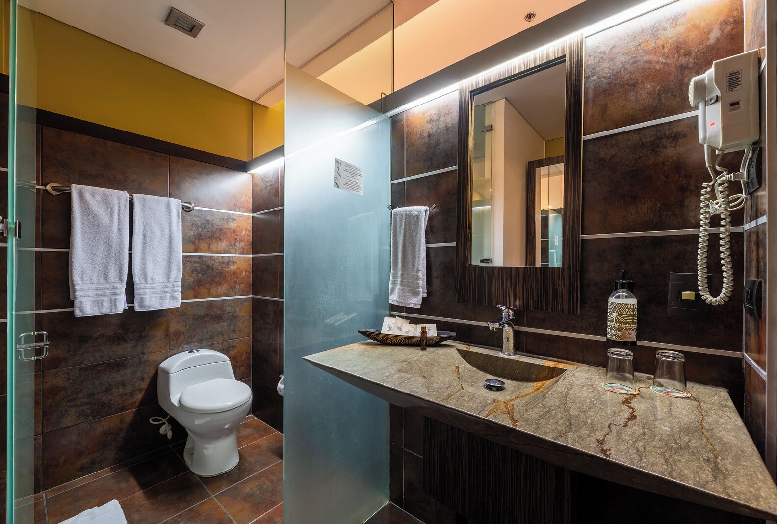 A modern bathroom with a glass partition, a white toilet, a marble sink, and a large mirror.