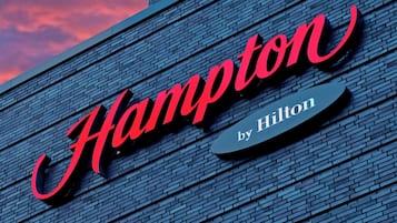 A hotel sign with the name "Hampton by Hilton" on a brick wall.