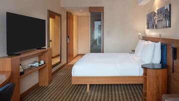 A hotel room with a large bed, a TV on a wooden stand, a desk, and a phone on a side table.