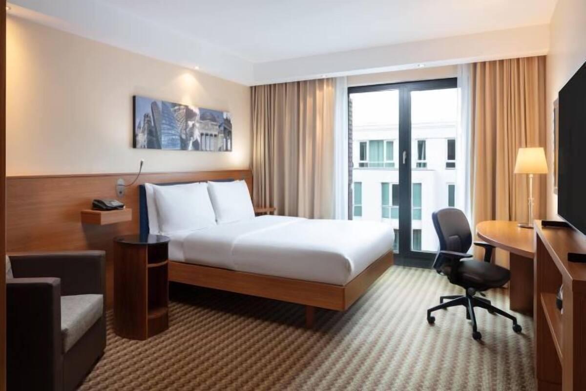 Une chambre d’hôtel équipée d’un lit, d’un bureau, d’une chaise, d’une télévision et d’une fenêtre avec des rideaux.