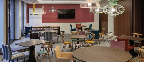 Un espace repas moderne doté de plusieurs tables et chaises, d’un téléviseur à écran plat fixé au mur et de luminaires décoratifs suspendus.