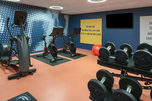 A gym with exercise equipment, a motivational quote on the wall, and a television.
