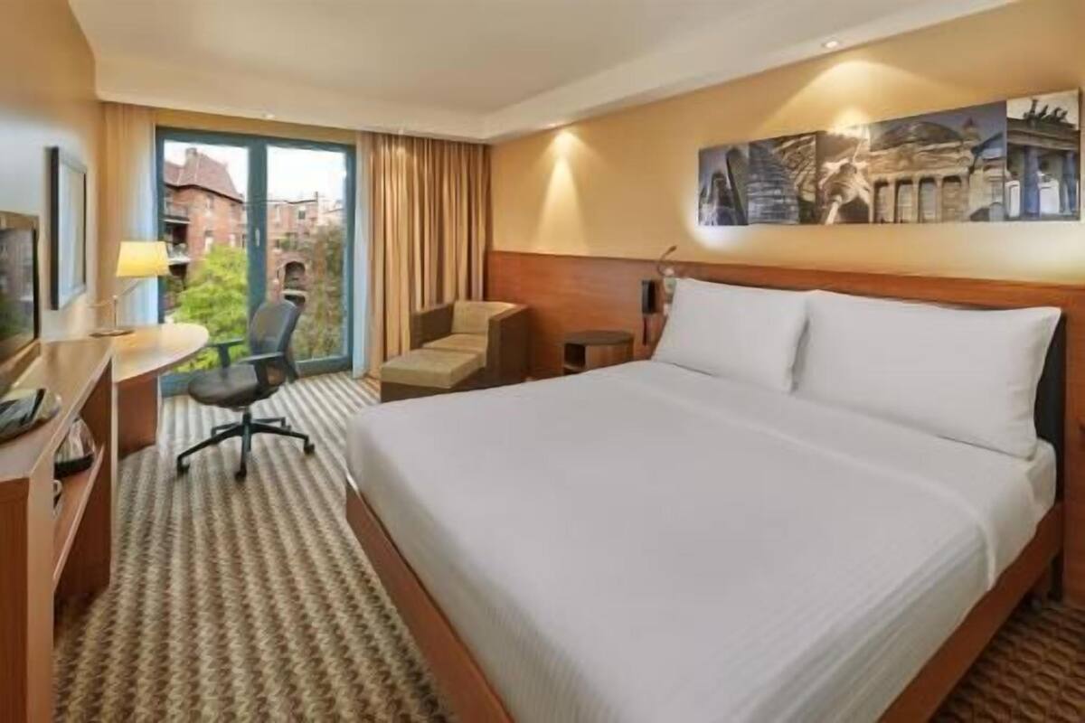Une chambre d’hôtel avec un grand lit, un bureau avec une chaise, une télévision et une fenêtre avec des rideaux.