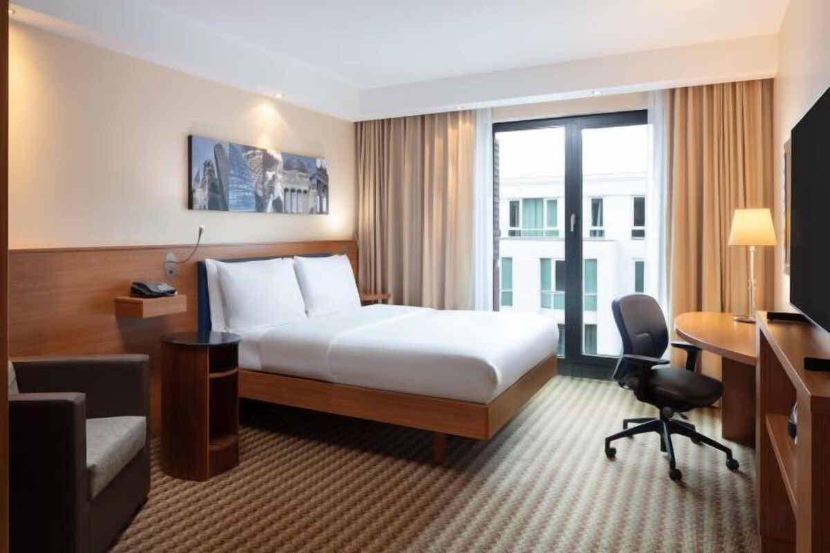 Une chambre d’hôtel équipée d’un lit, d’un bureau, d’une chaise, d’une télévision et d’une fenêtre avec des rideaux.