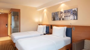 Ett hotellrum med två sängar, en sänggavel i trä, en liten sittgrupp och ett konstverk som hänger på väggen.