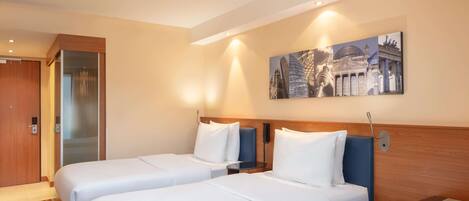 A hotel room with two beds, a wooden headboard, a small seating area, and a wall-mounted artwork.