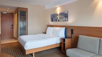 Ein Hotelzimmer mit einem Bett, einer Couch, einem Gemälde an der Wand und einer Holztür.