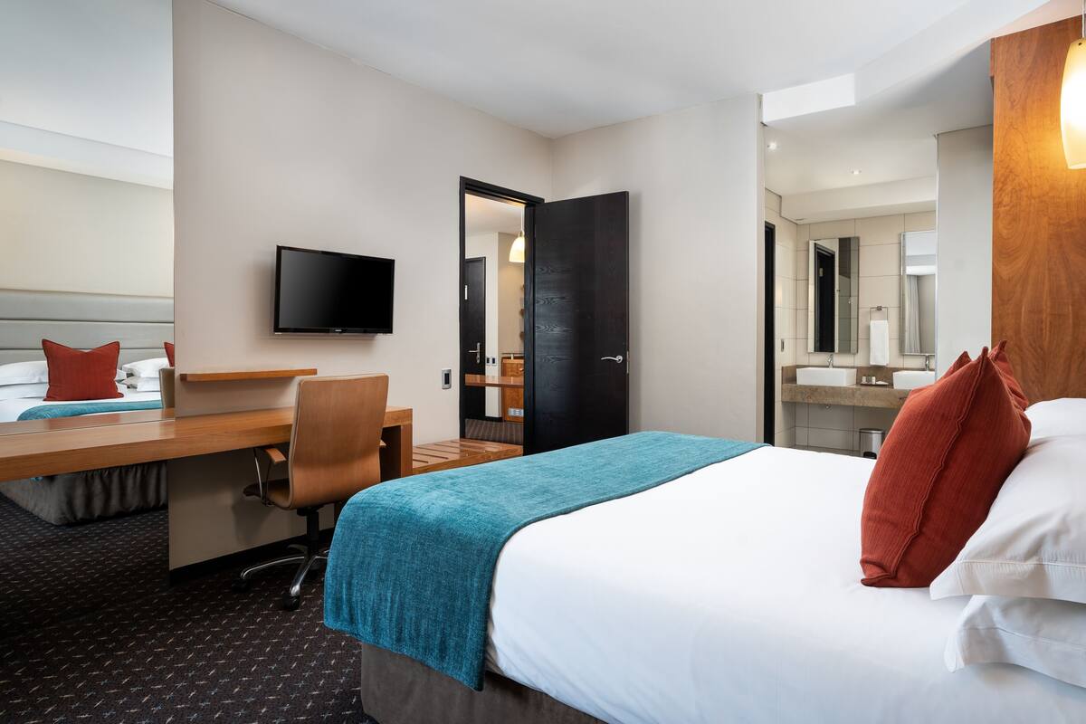 A hotel room with a bed, desk, chair, television, and a bathroom visible through an open door.