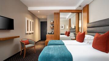 Quarto de hotel com uma cama grande, uma cadeira, uma televisão e uma escrivaninha com abajur.