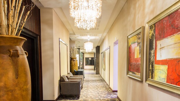 Un pasillo de hotel con alfombra estampada, un jarrón grande, obras de arte enmarcadas y un candelabro.