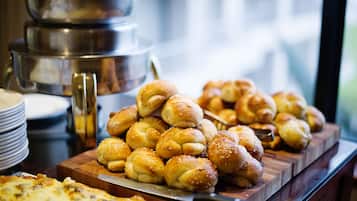 A buffet table with various baked goods, including bread rolls and a pizza.