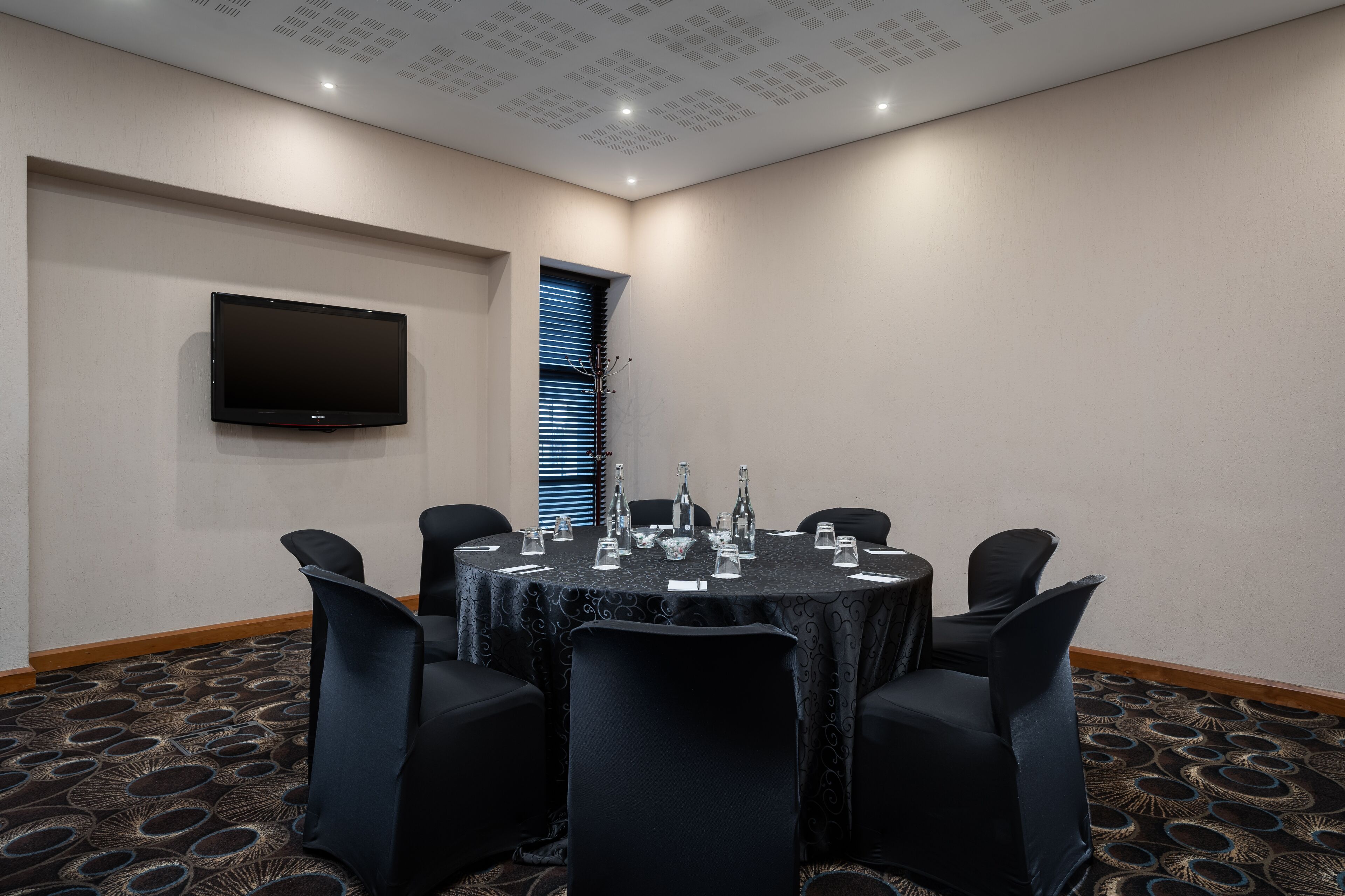 A conference room with a round table, black chairs, and a flat-screen TV mounted on the wall.