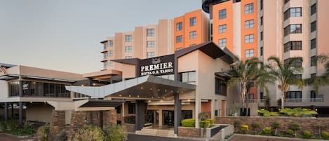 Un hotel con una entrada destacada, varios pisos y un cartel que indica que es el Premier Hotel O.R. Tambo.