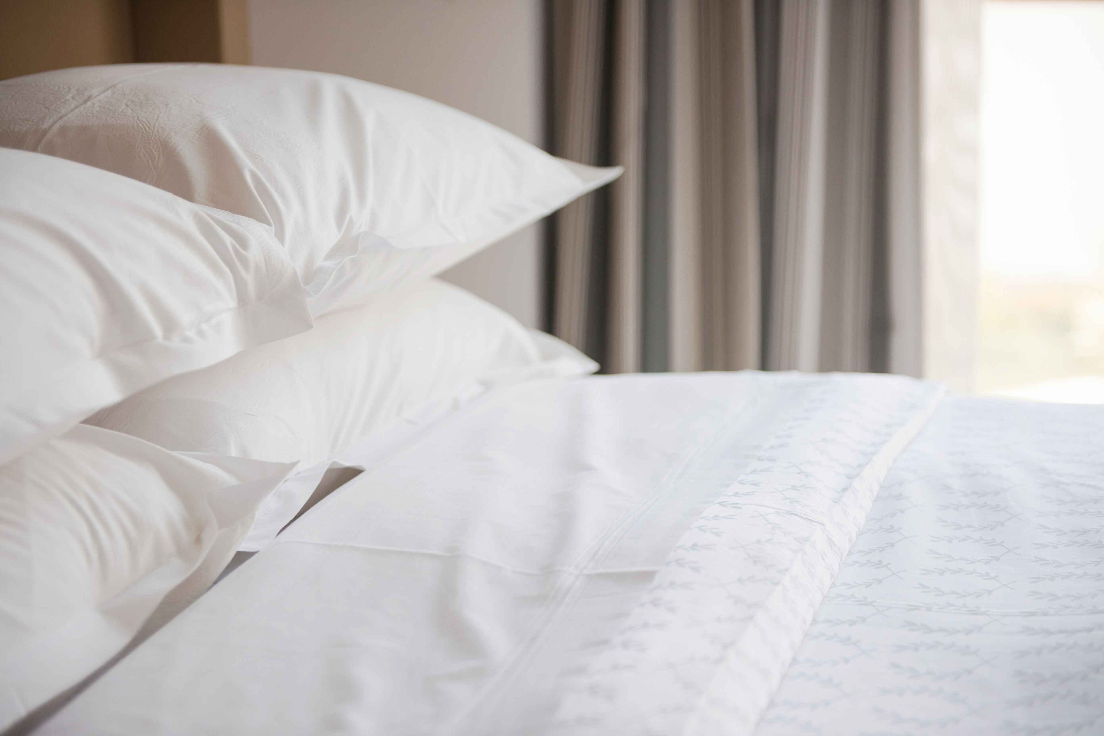 A neatly made bed with white linens and a subtle pattern.