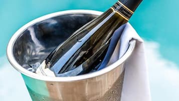 A champagne bottle in a metallic bucket with a white napkin, placed by a pool.