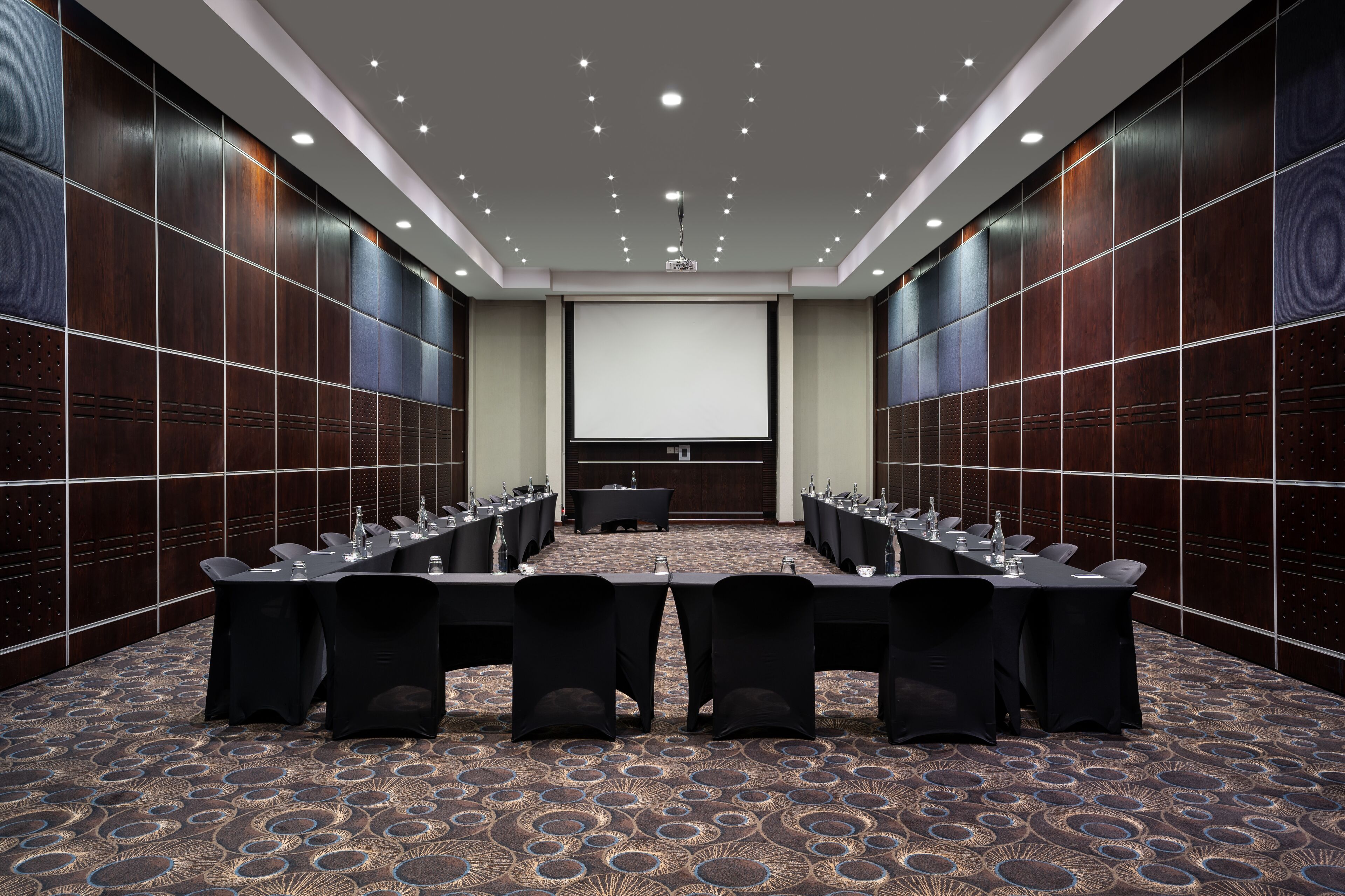 A conference room with a long table, chairs, a projector screen, and a reception desk.