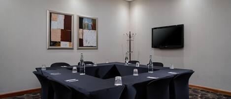 Un salón de conferencias con una mesa grande, sillas, un televisor y obras de arte en las paredes.