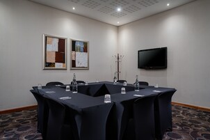 Un salón de conferencias con una mesa grande, sillas, un televisor y obras de arte en las paredes.