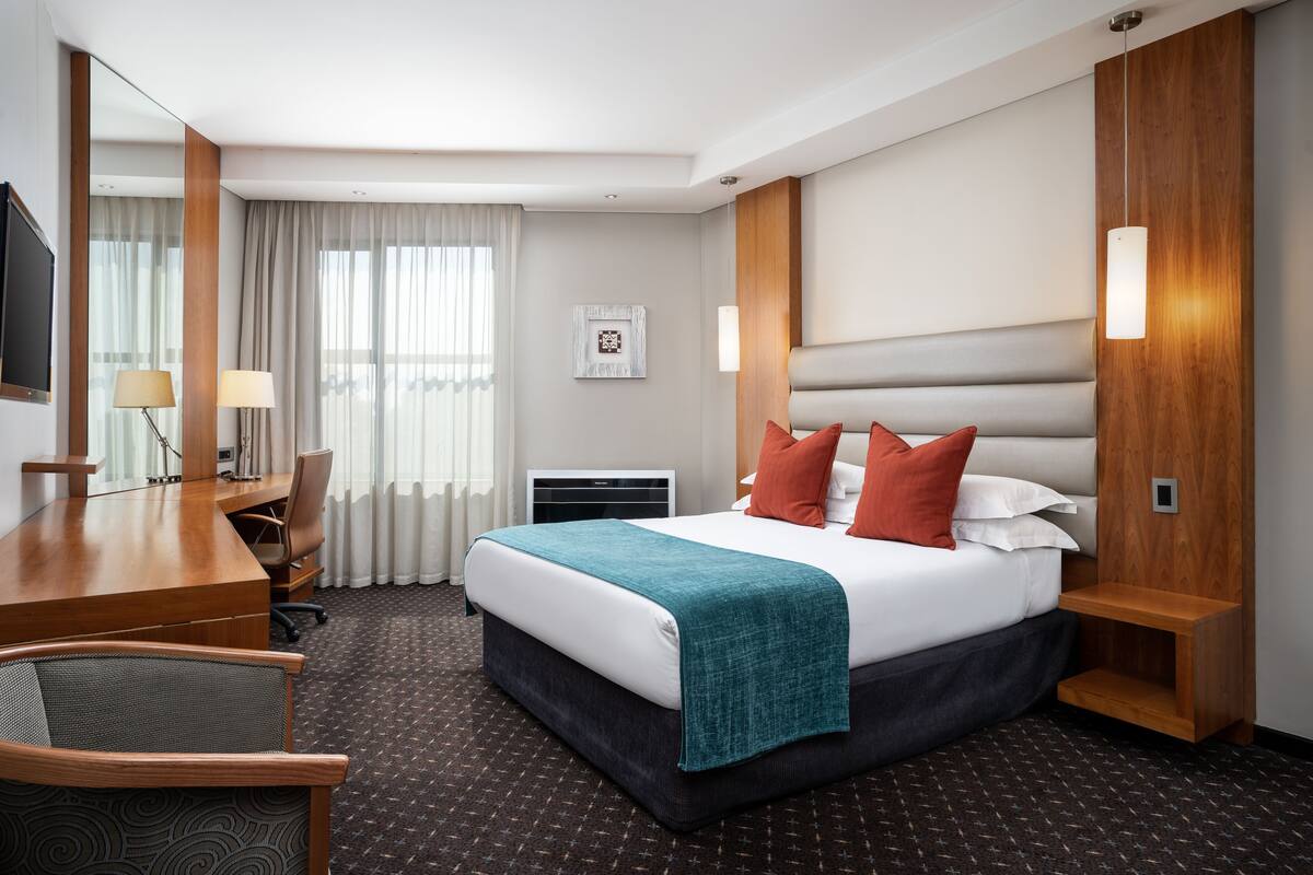 A hotel room with a bed, a desk, a chair, a TV, and a window with curtains.