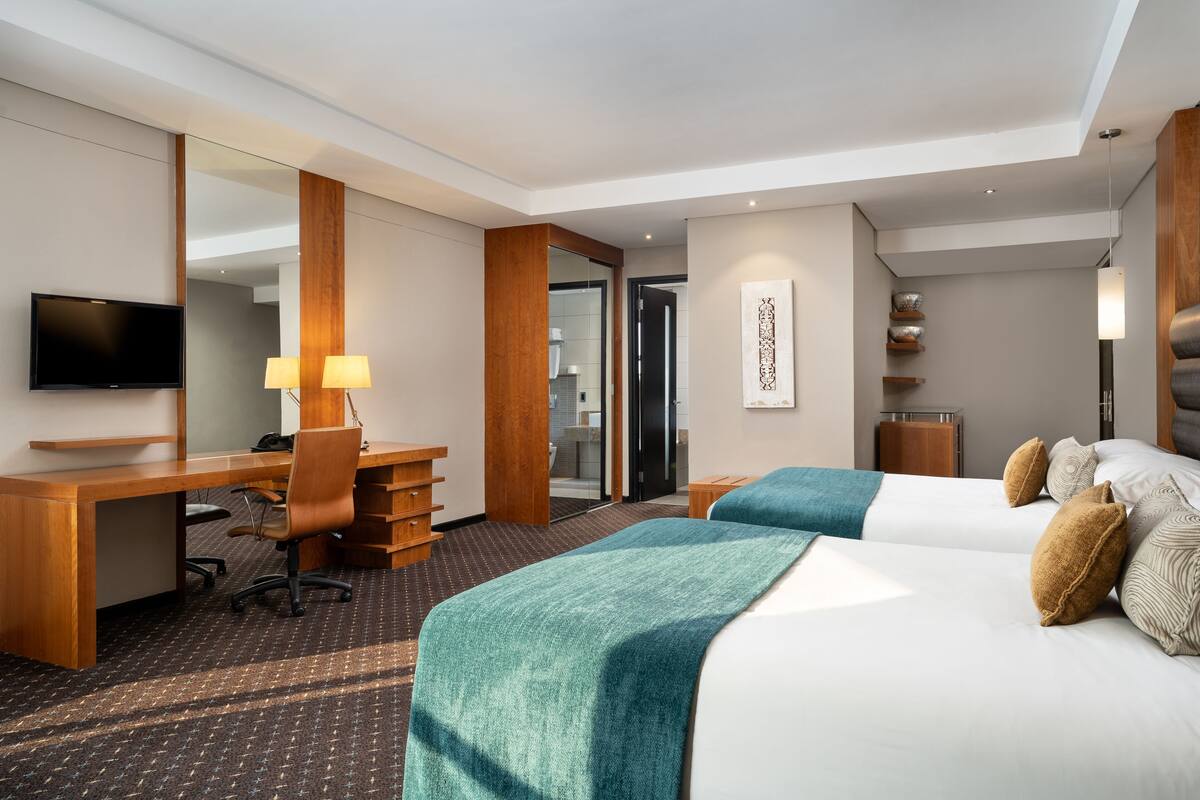 A hotel room with a desk, two beds, a TV, and a large mirror.
