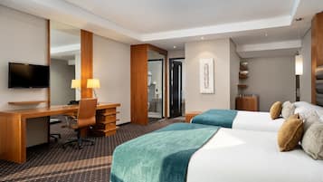 Habitación de hotel con escritorio, dos camas, televisor y un espejo grande.