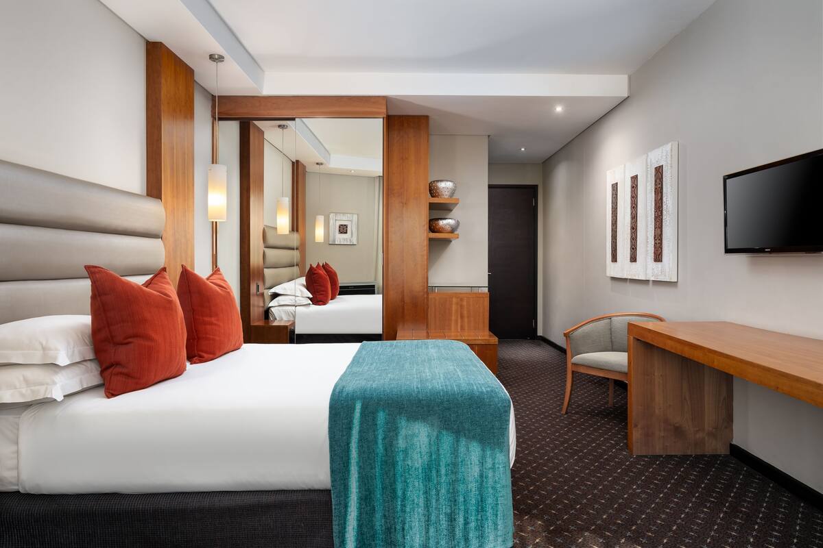 A modern hotel room with a large bed, a desk, and a television.