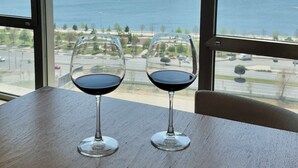 Dos copas de vino sobre una mesa de madera, junto a una ventana grande con vista a un cuerpo de agua y tierra distante.