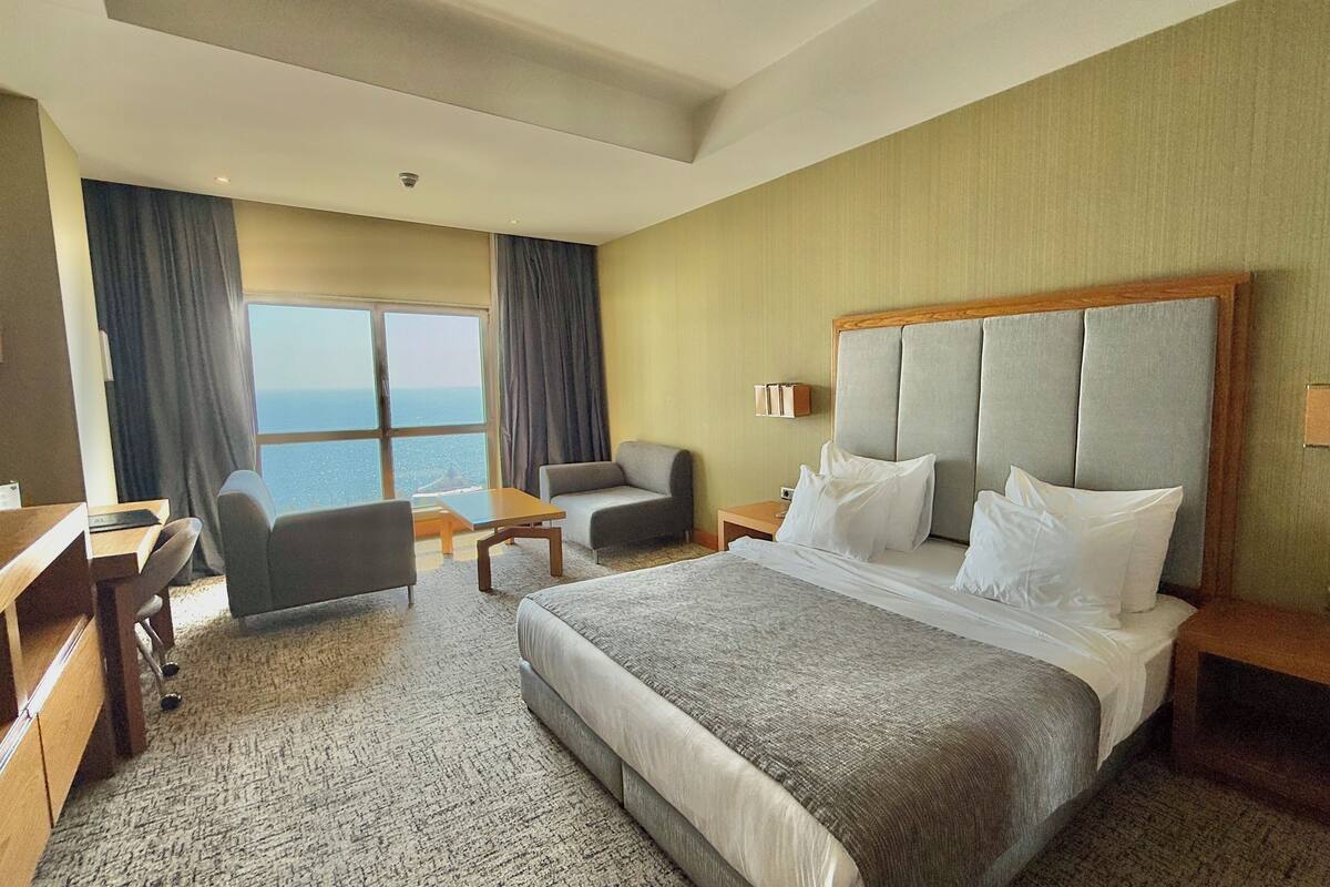 Ein Hotelzimmer mit einem großen Bett, einem Schreibtisch, einem Stuhl und Meerblick.