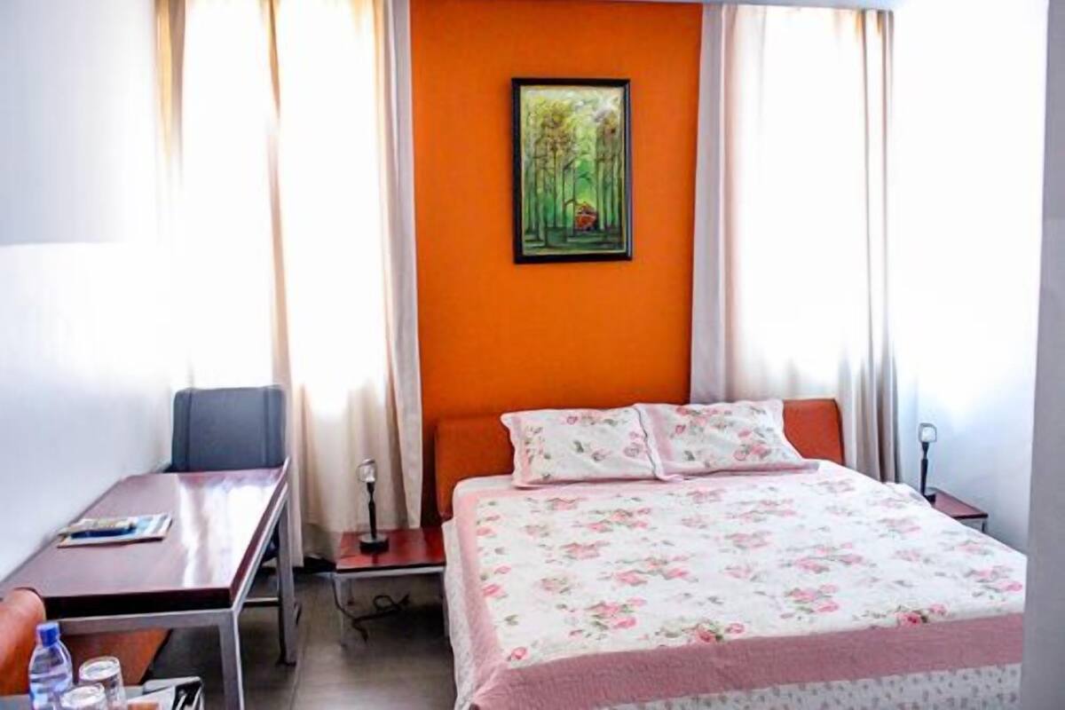 A hotel room with a bed, a desk, and a painting on the wall.
