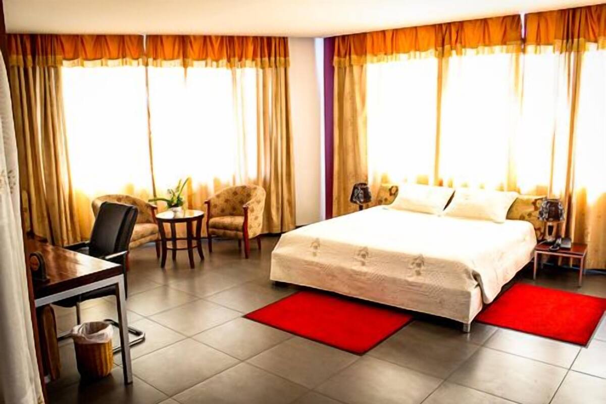 A hotel room with a bed, a desk, a chair, and a small table.