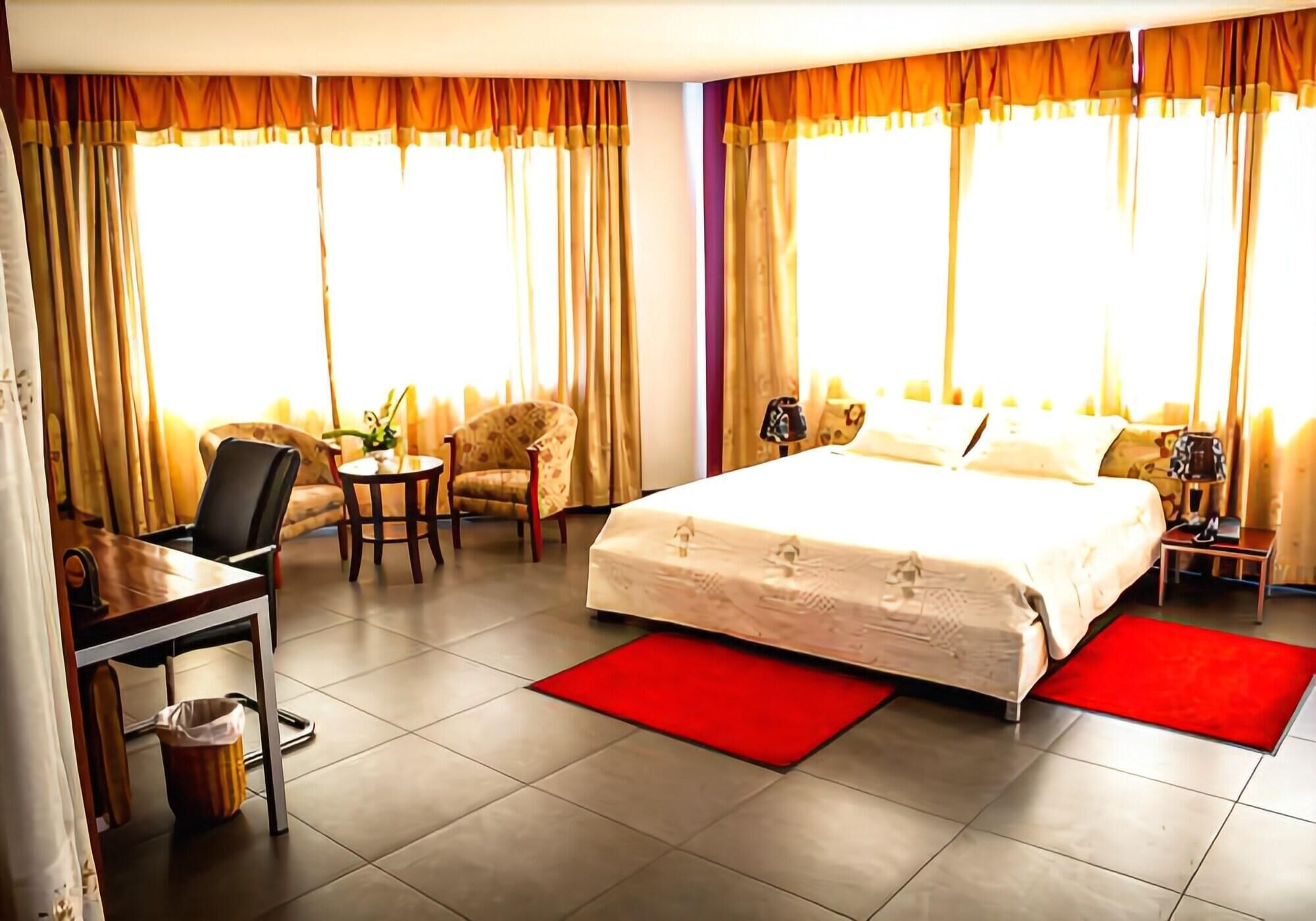 A hotel room with a bed, a desk, a chair, a small table, and curtains.