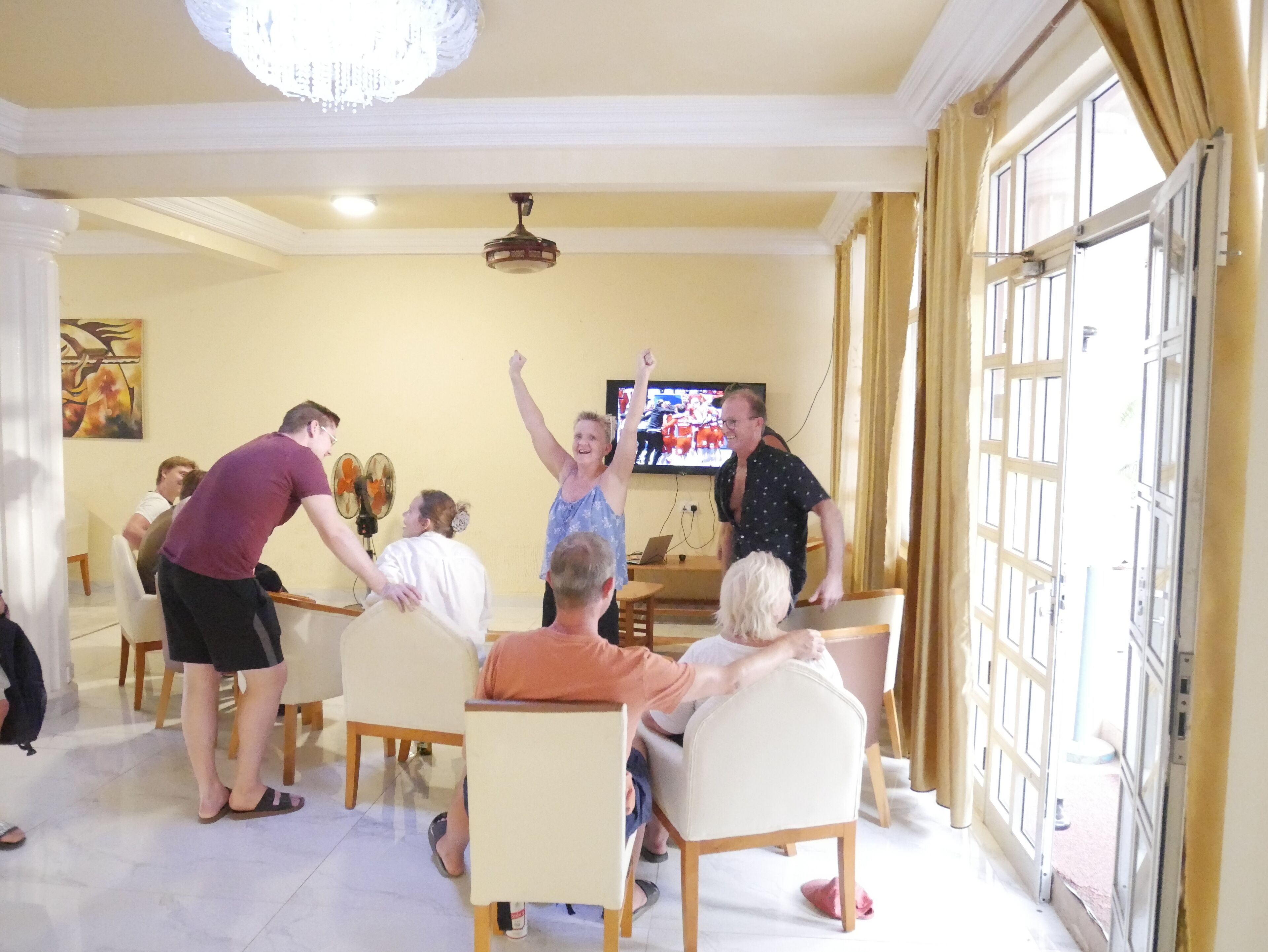 Een groep mensen in een kamer met een televisie, stoelen en een tafel.