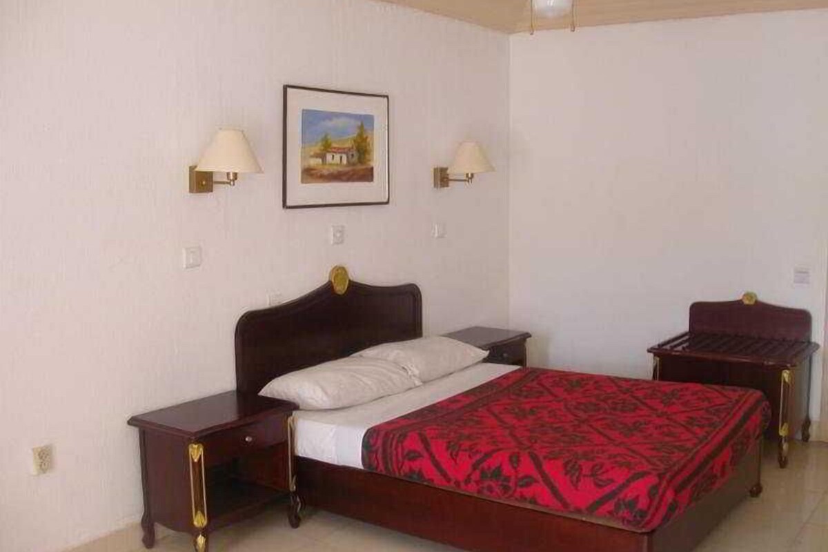 A bedroom with a bed, two bedside tables, a nightstand, a lamp, and a framed picture on the wall.