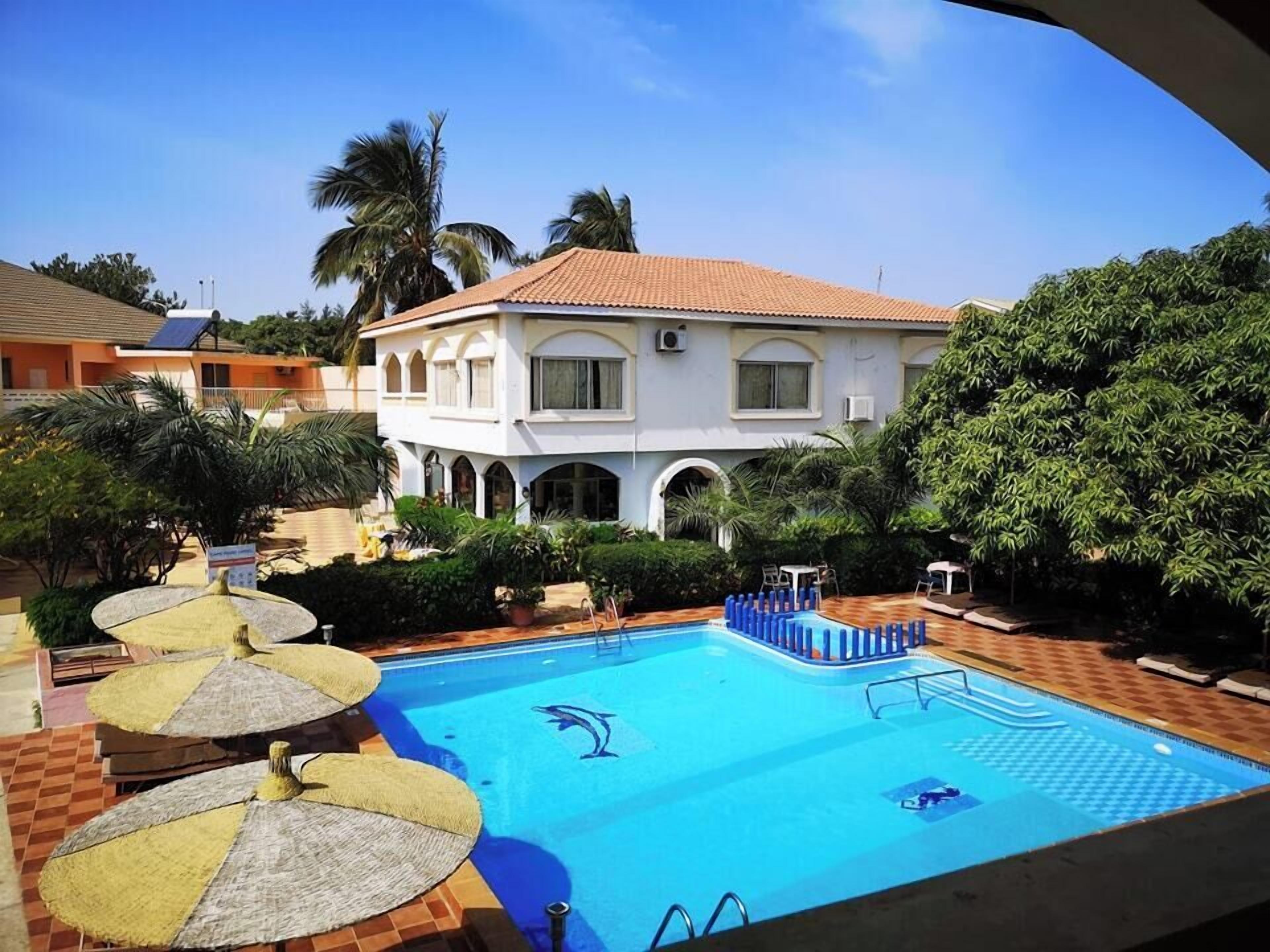 A swimming pool with a dolphin logo, surrounded by palm trees and a white building with arched windows.