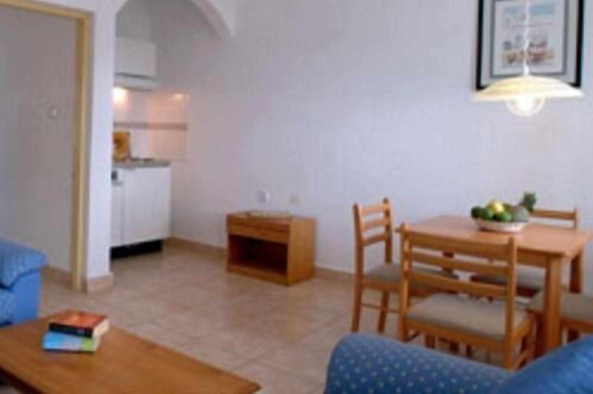 Een compacte woonruimte met een kitchenette, een eethoek met houten meubels en een klein zitgedeelte.