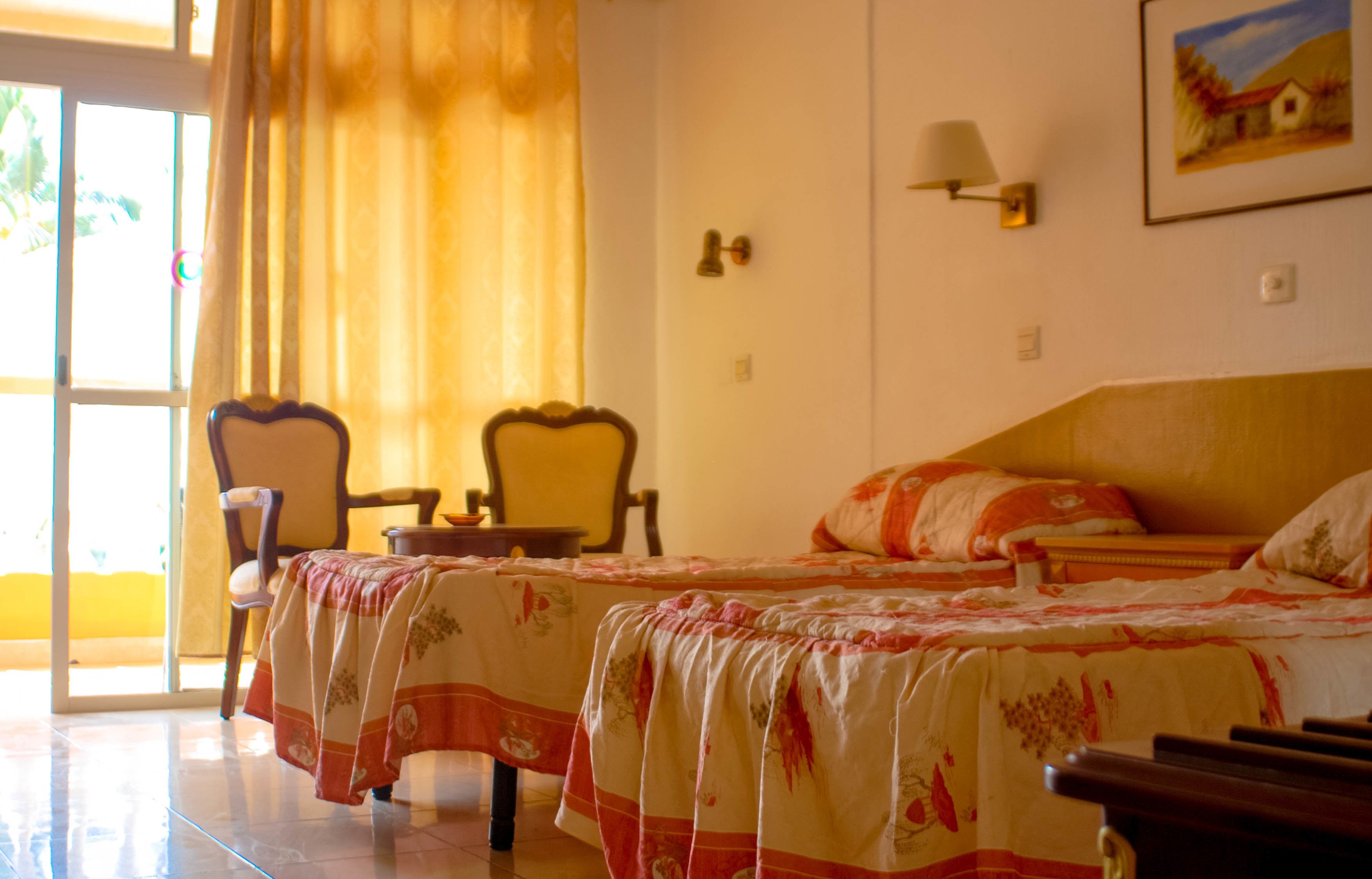 A hotel room with two beds, a chair, a table, and a window with curtains.