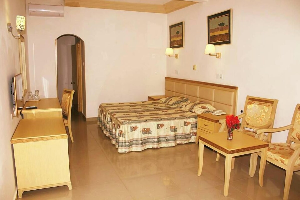 A hotel room with a bed, bedside table, chair, desk, and a mirror.