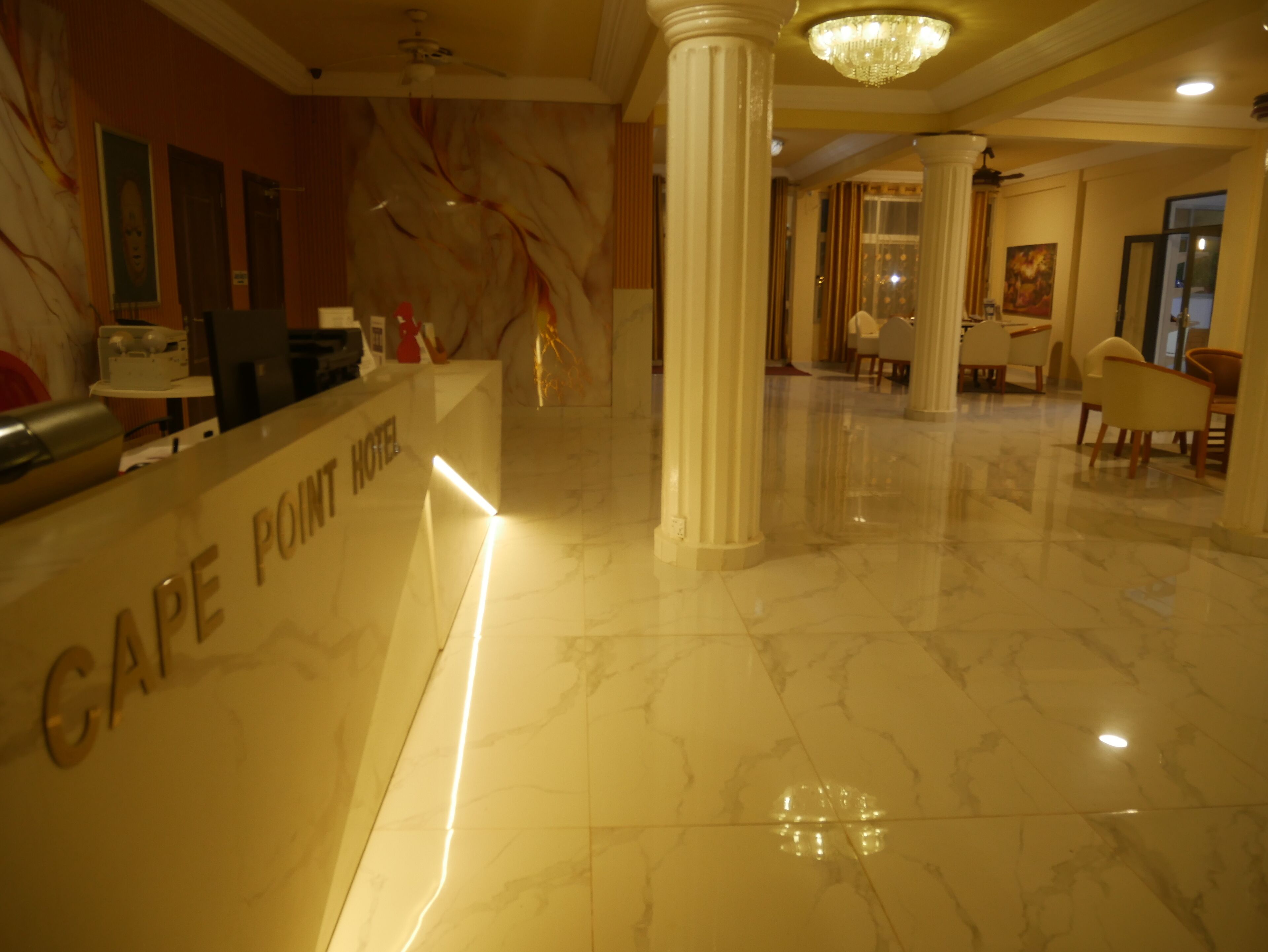 A hotel lobby with marble floors, a reception desk, and a chandelier.