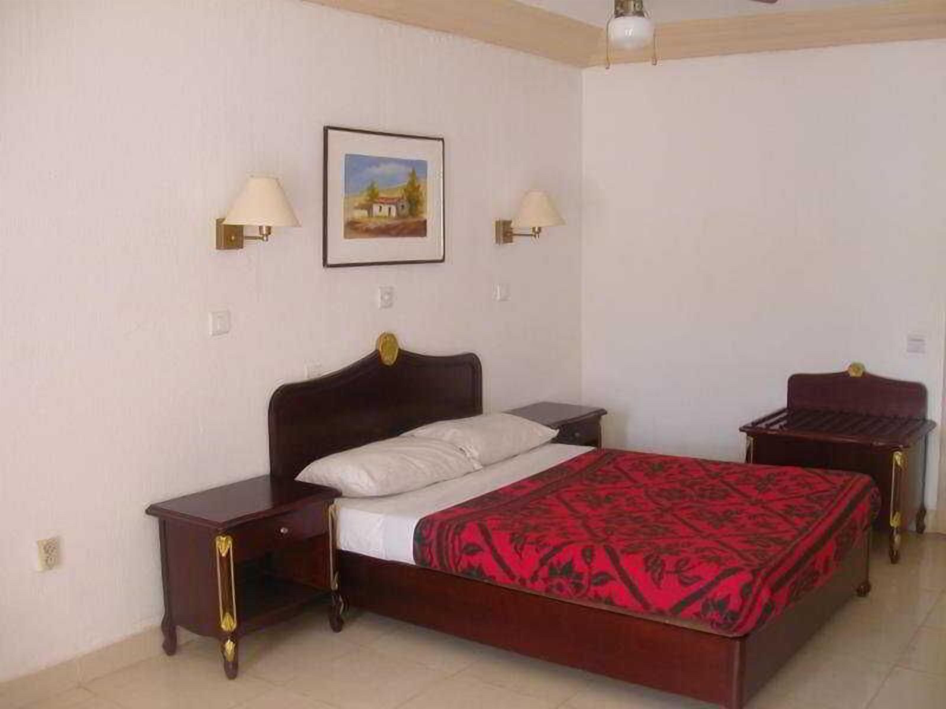 A bedroom with a bed, two bedside tables, a nightstand, a lamp, and a framed picture on the wall.