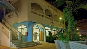 Entrada de hotel con escaleras, ventanas de arco y plantas en macetas.