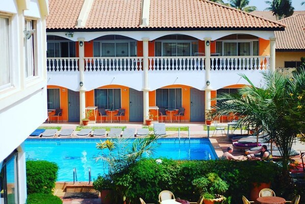 Un hotel con piscina, mobiliario exterior y un balcón con detalles en naranja.