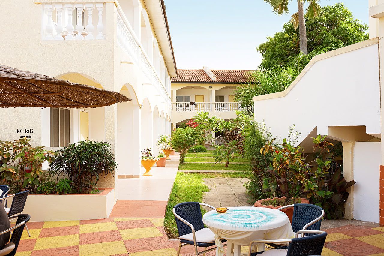 Une cour avec un espace repas, des plantes en pot et un bâtiment blanc doté de balcons.