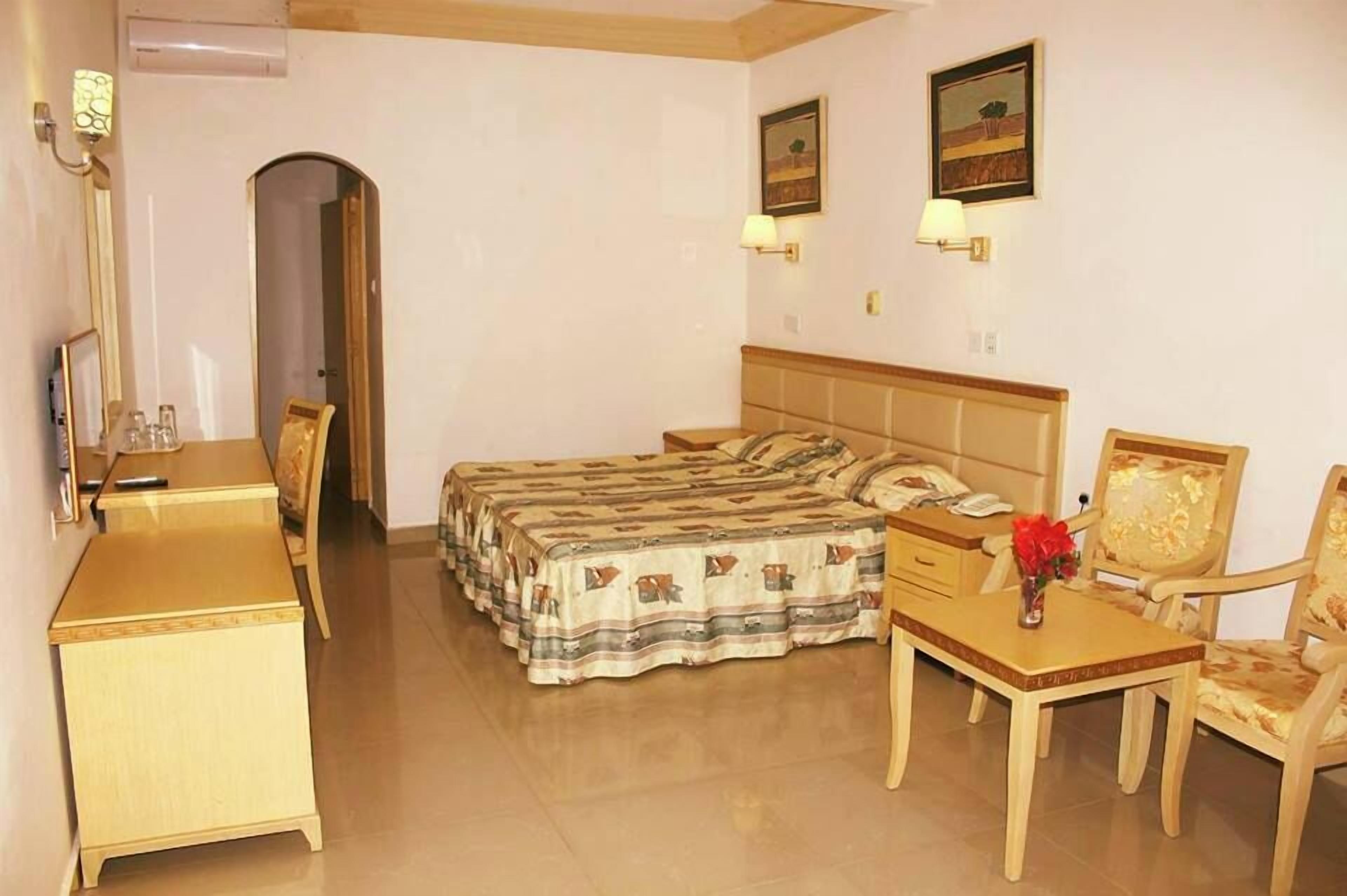 A hotel room with a bed, a desk, a chair, a lamp, and a picture on the wall.