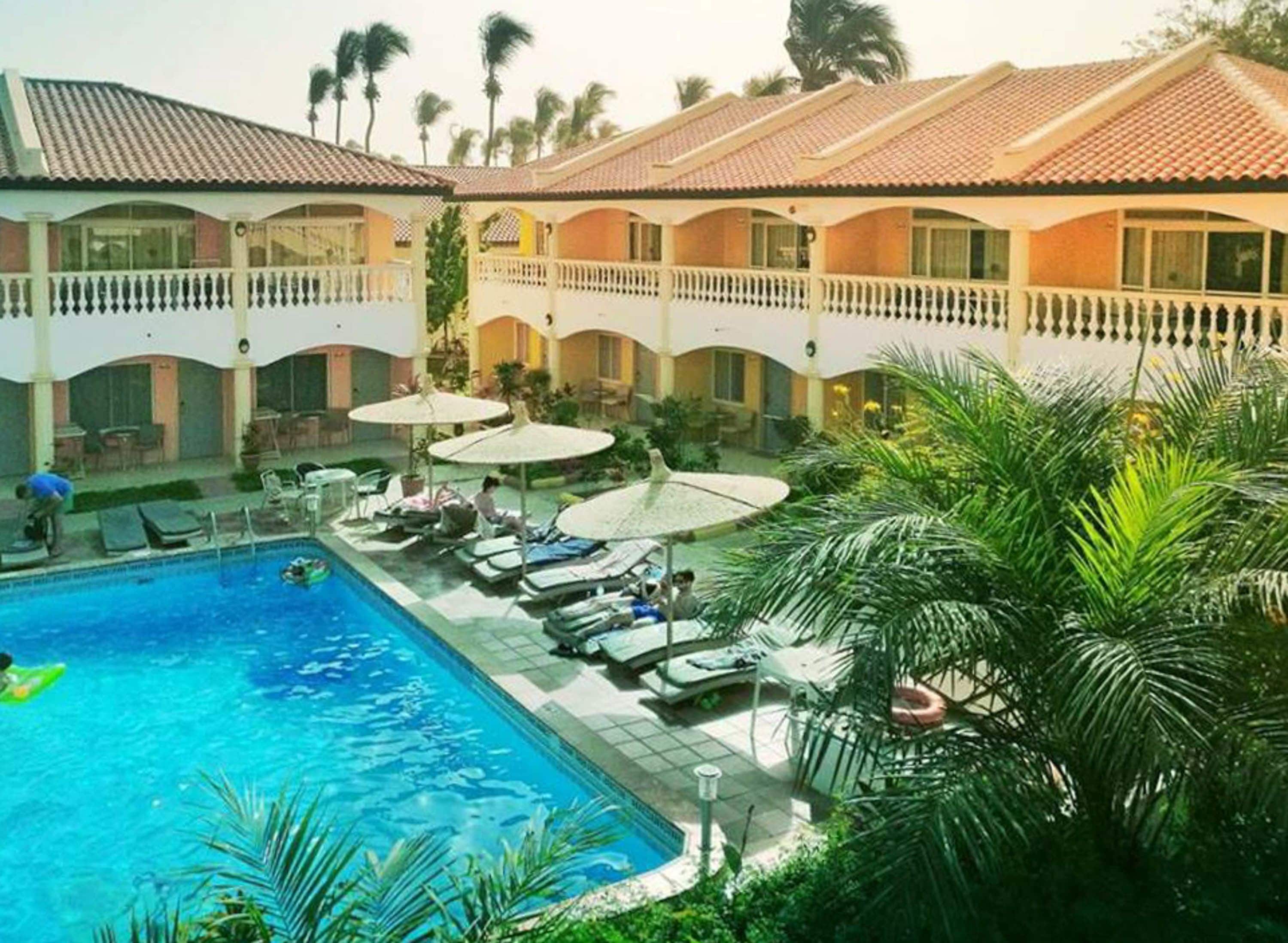 Un hotel con piscina, sillas de descanso y sombrillas.
