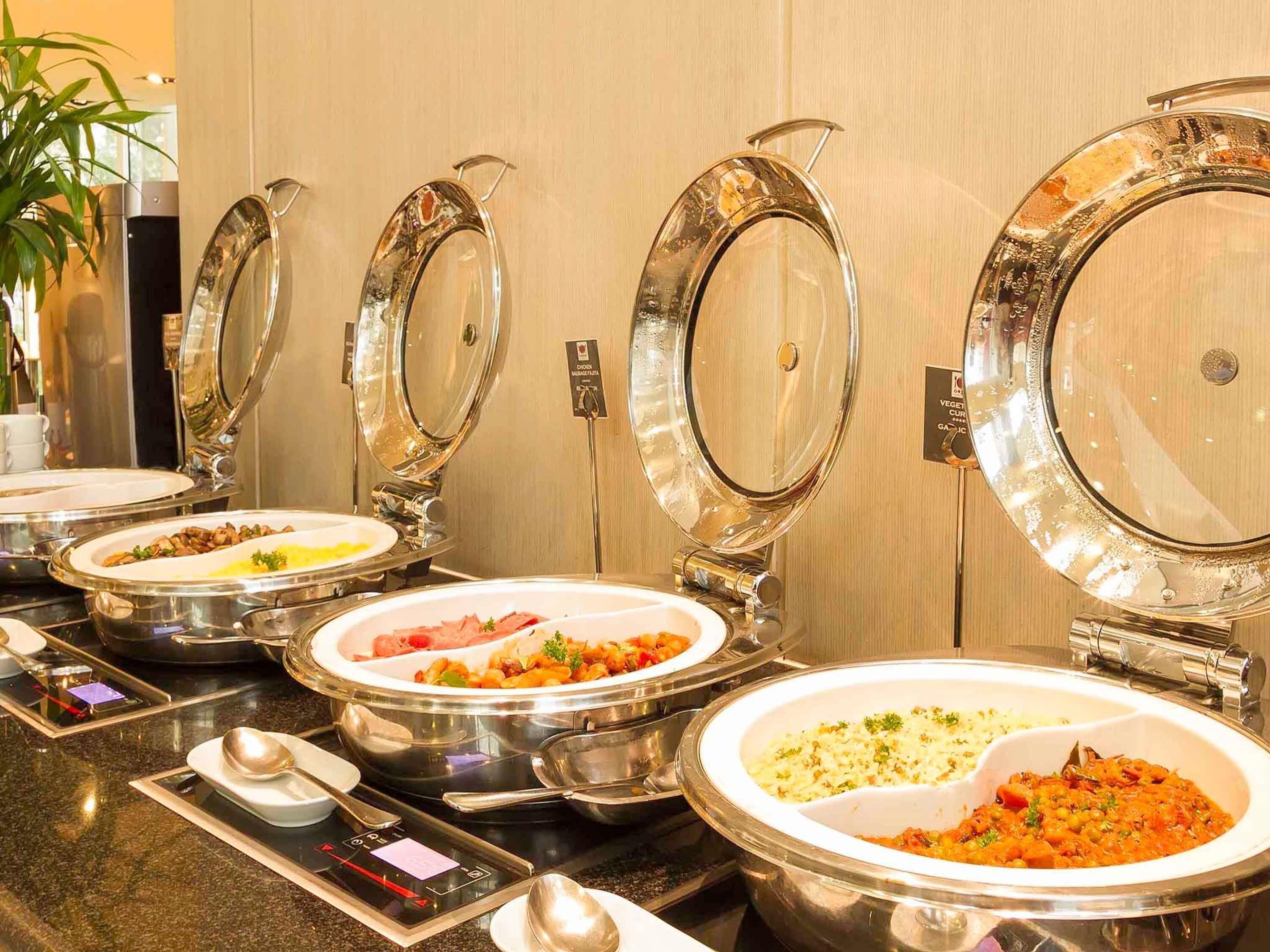 Estaciones de comidas tipo buffet con tapas transparentes y fuentes de acero inoxidable.