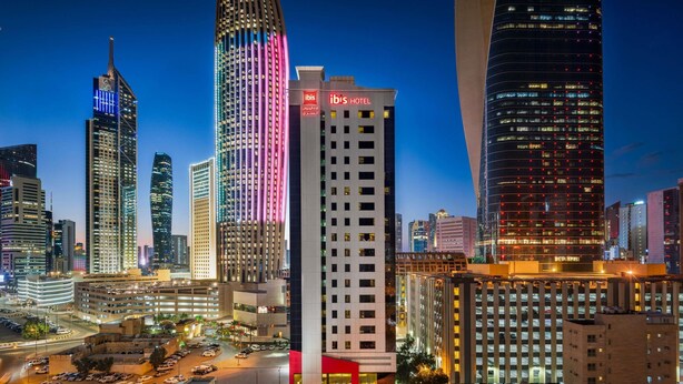 A cityscape with modern buildings, including a hotel with a prominent red and white sign. - ibis Sharq Kuwait (Kuwait City)
