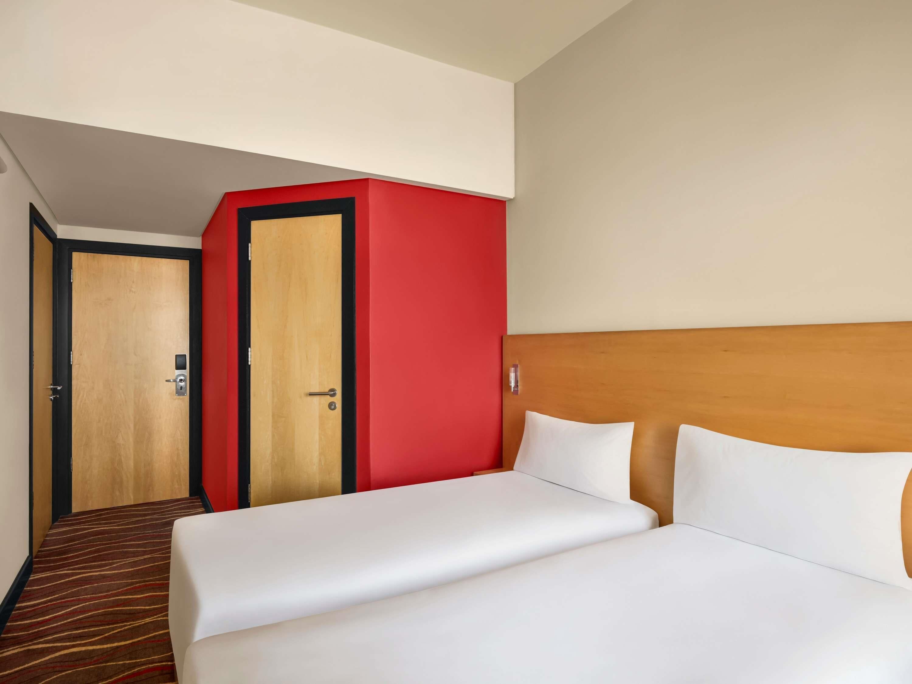 A hotel room with a bed, a red wardrobe, and a carpeted hallway.