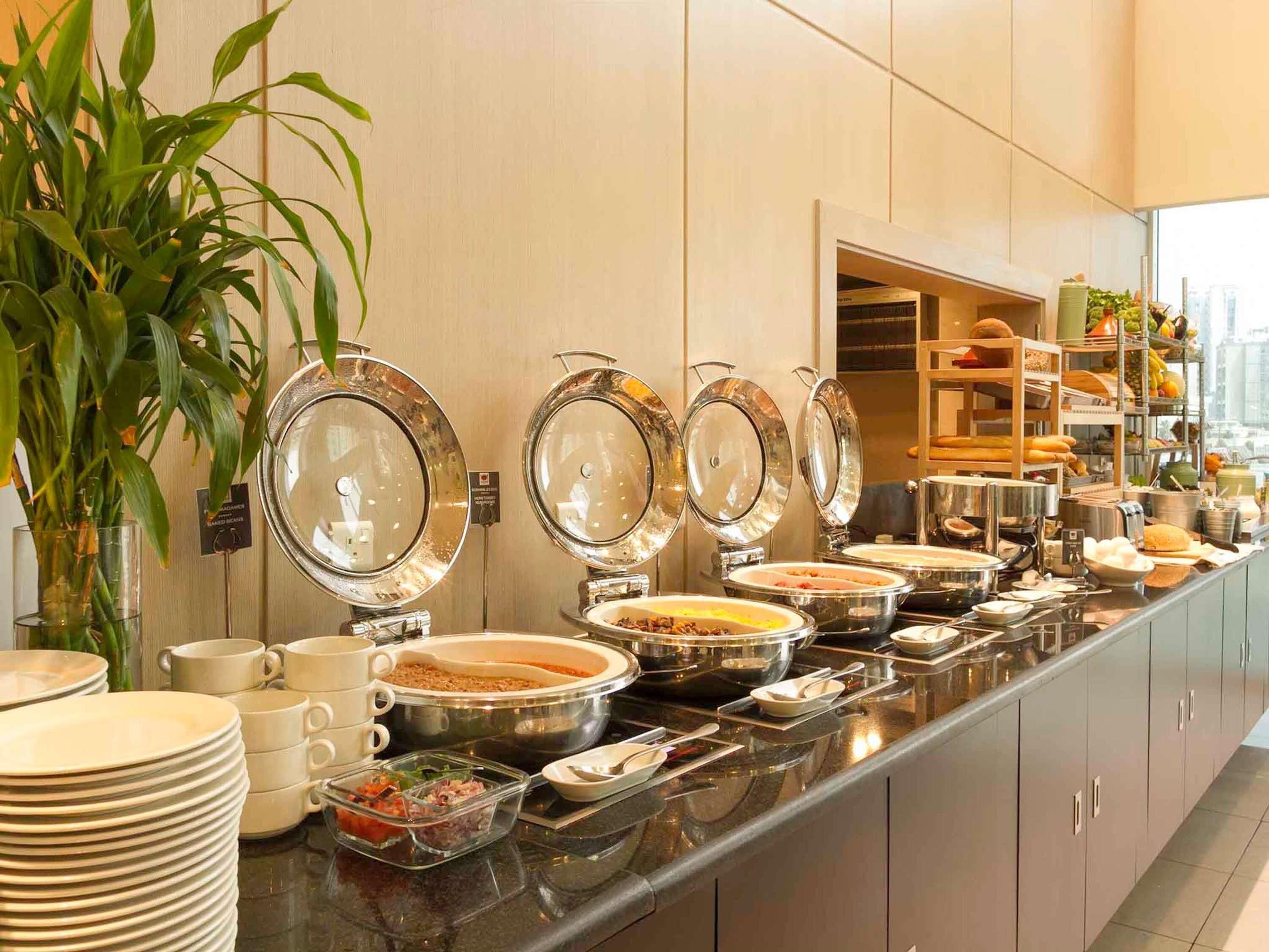 A buffet setup with various food containers, a plant, and a view of the city.