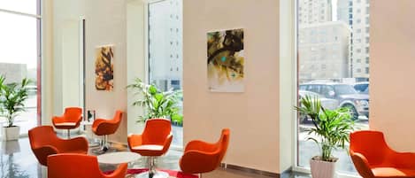 Un moderno vestíbulo de hotel con sillas naranjas, una alfombra roja y grandes ventanales que ofrecen vistas de la ciudad.