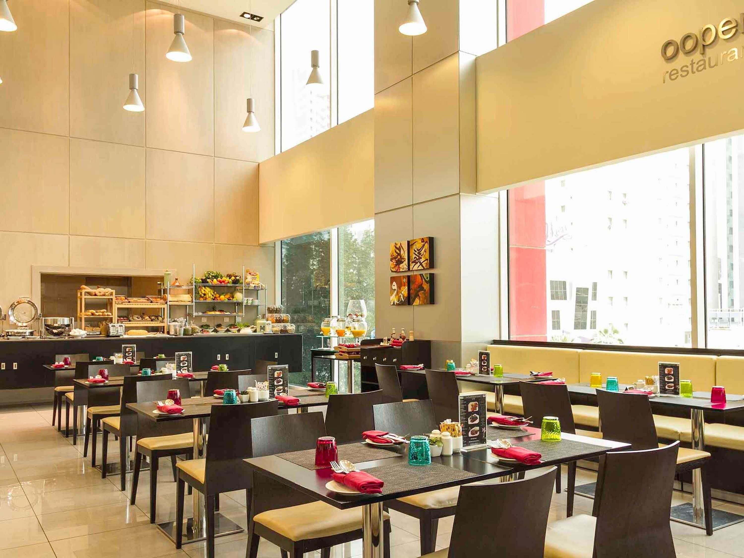 Restaurante moderno com área de buffet, mesas e cadeiras dispostas para os hóspedes.